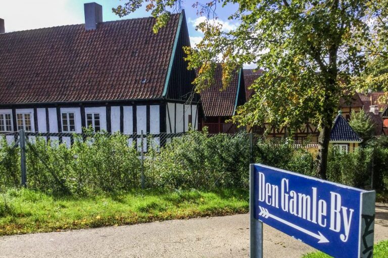 Den Gamle By:n kyltti ja taustalla vanha rakennus.