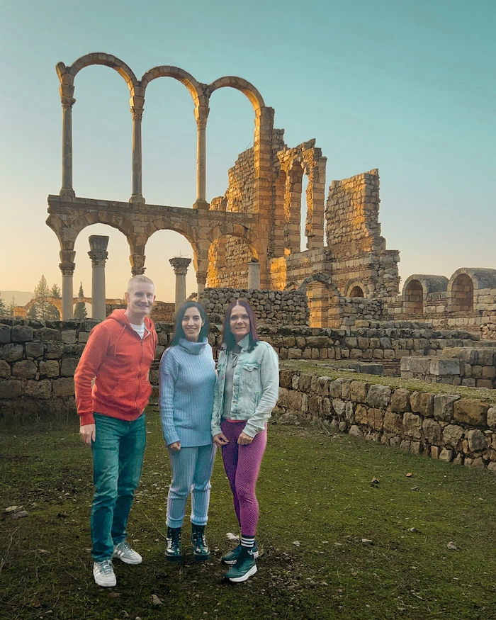 Kolme henkilöä temppeliraunioiden edessä ilta-auringossa.